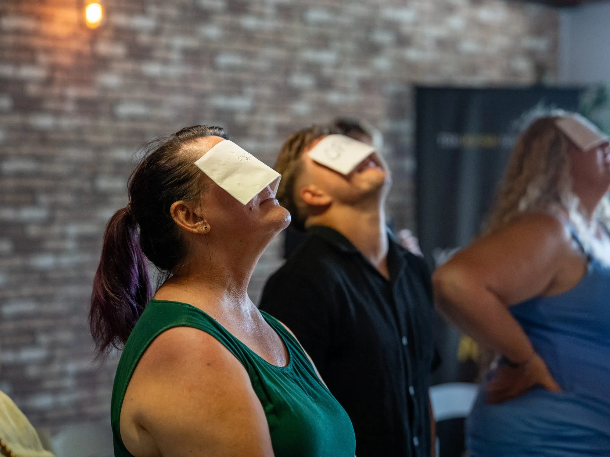 Participants standing with cards on their foreheads, eyes turned upward, during a live exercise