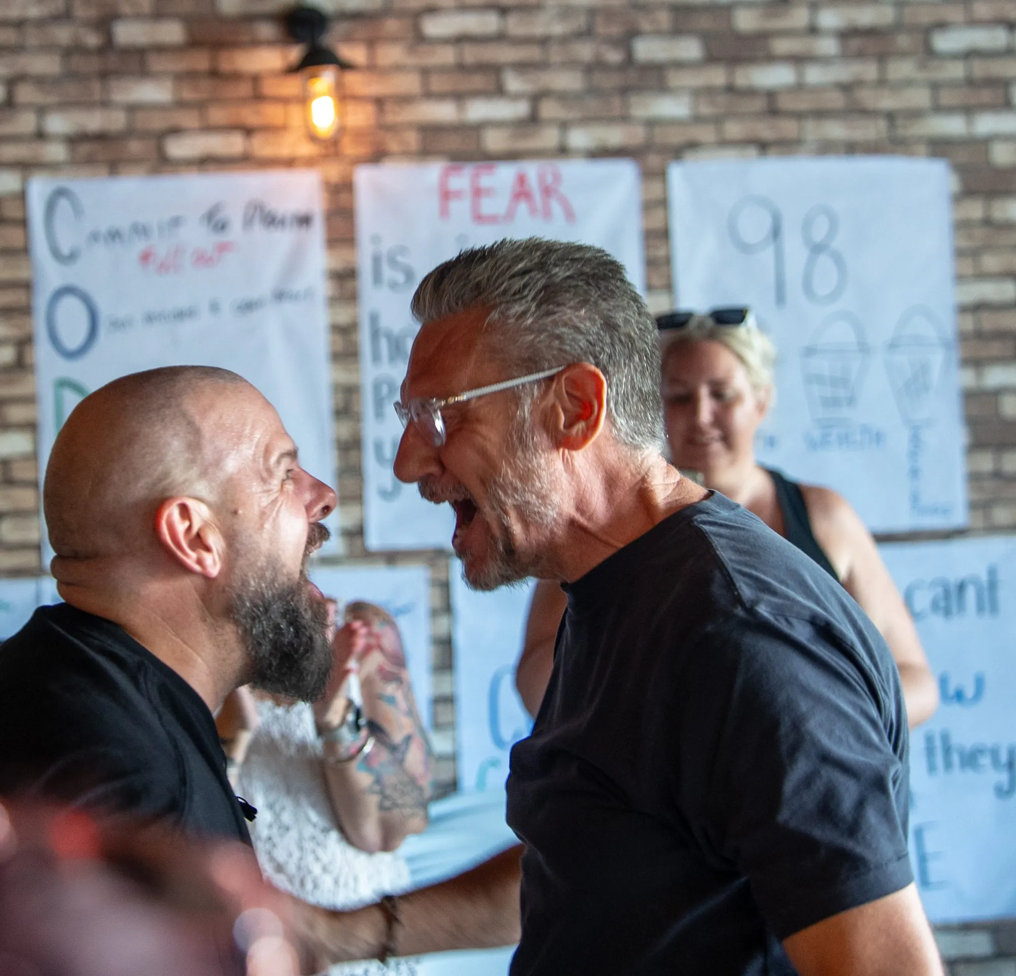 Brett face to face with a participant in an intense, animated exchange, handwritten posters behind them