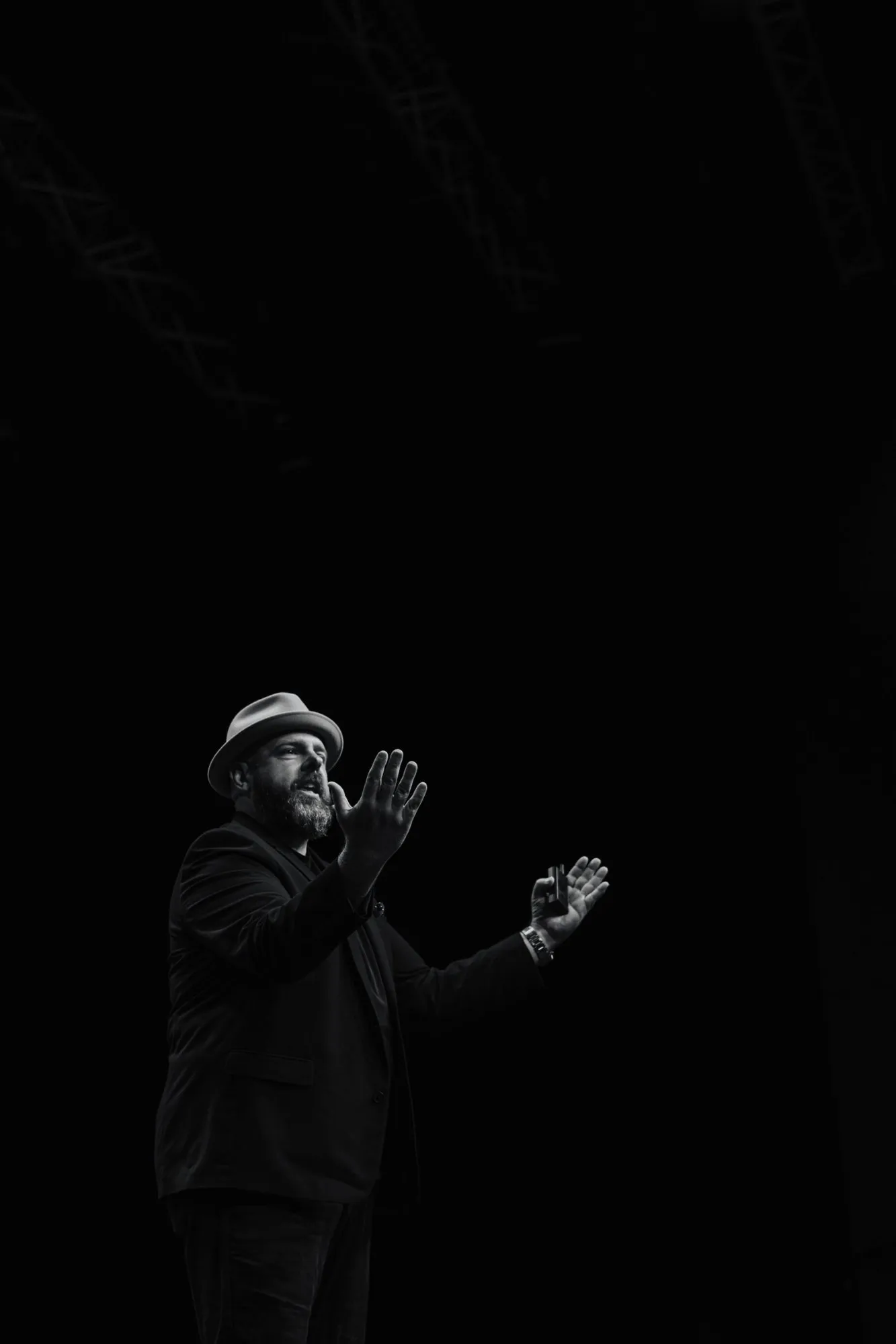 Black and white photo of Brett on stage in a fedora, hands raised mid-sentence