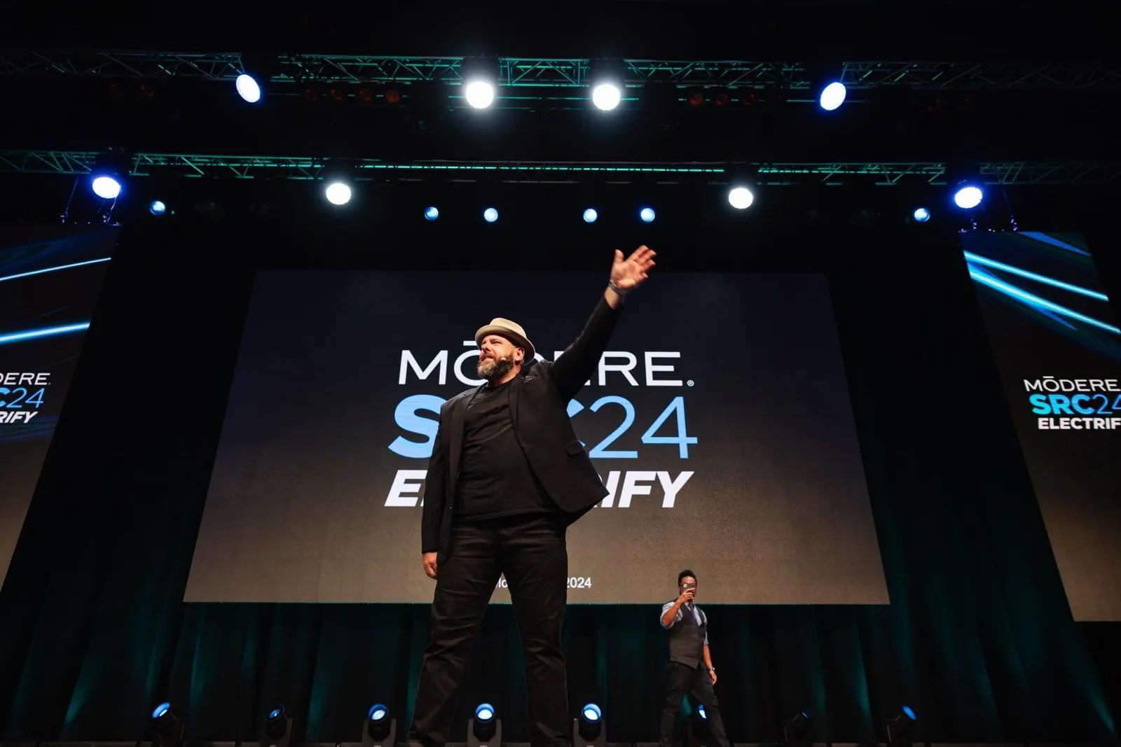 Brett waving to the audience at the front of a conference stage