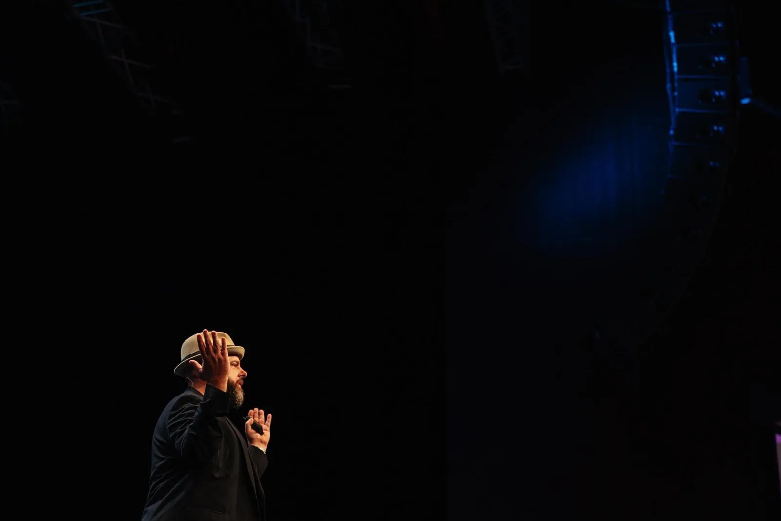 Brett in profile mid-gesture on a dark, wide stage