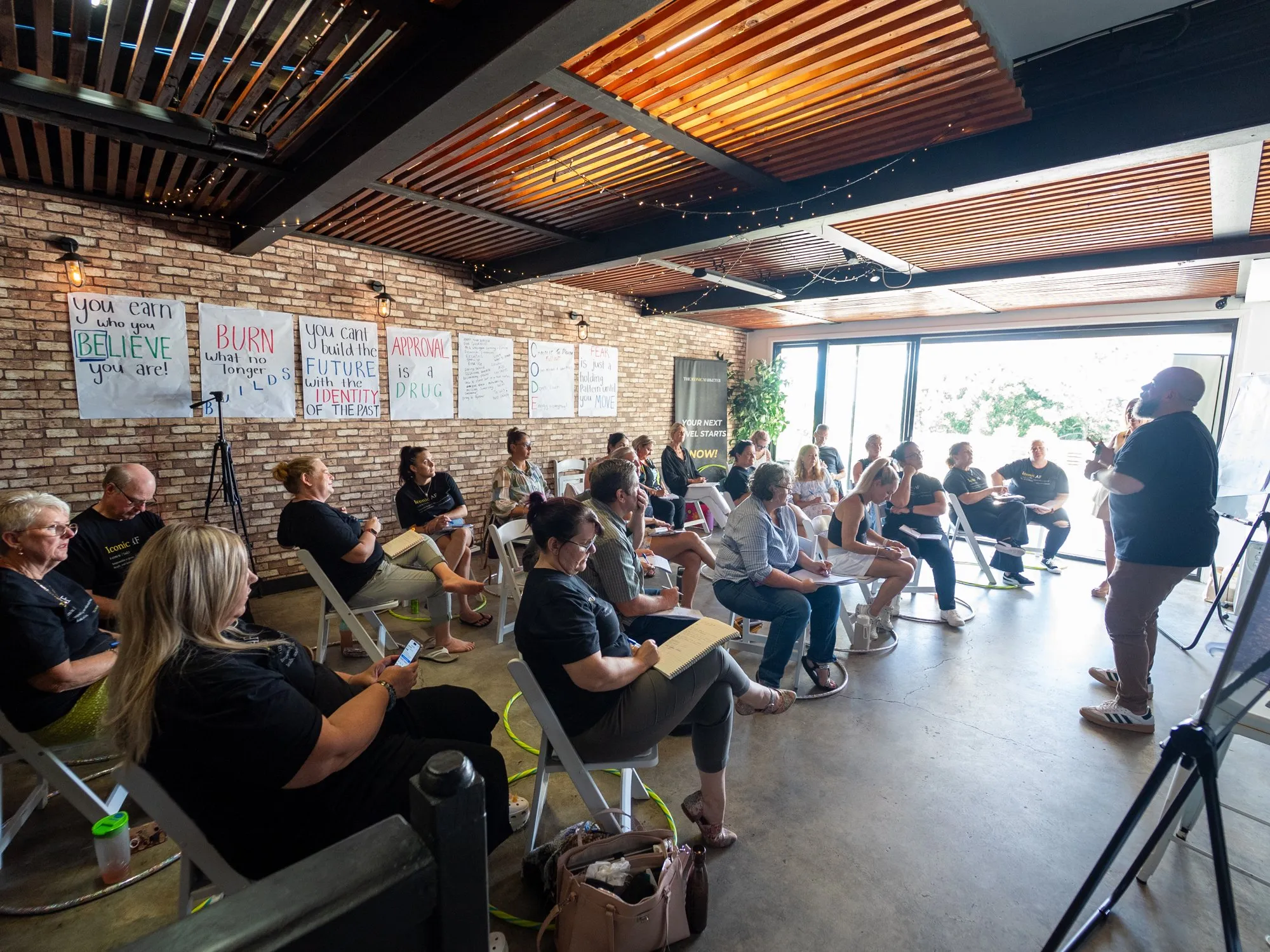 Brett presenting to a full workshop room, participants seated with notes, flipchart pages on the brick walls